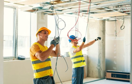 Side view at two construction crew workers separated by wall while renovating house, copy space. portrait of young people electrician connecting cables in wires cabinet while renovating house, copy space